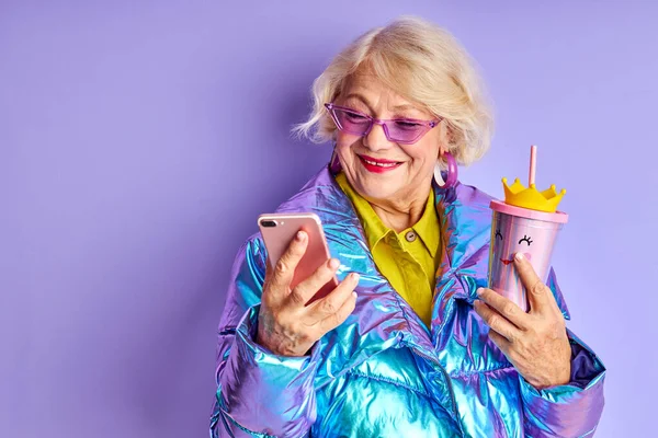 excited elderly woman with mobile phone posing at camera