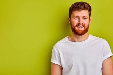 Günlük tişörtlü genç beyaz adam kameraya gülümsüyor.