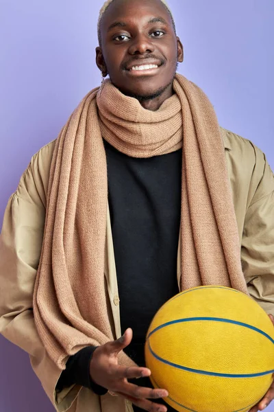 Portrait of afro american guy in coat and scarf posing with basketball ball — Stockfoto