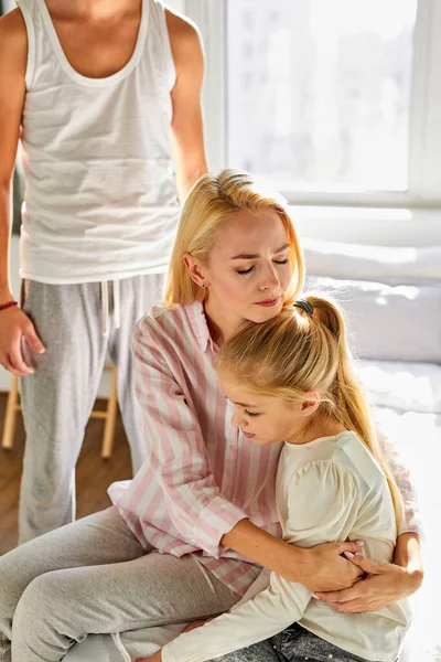 En kvinna sätter sig med ett barn, lugnar ner henne medan en man svär på dem — Stockfoto