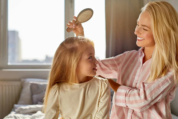Hermosa niña caucásica sonriendo mientras su madre peinándose el pelo —  Fotos de Stock