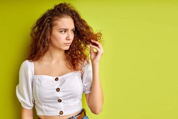 Pensativa chica rizada está mirando puntas abiertas de pelo —  Fotos de Stock