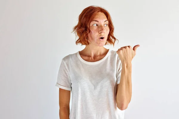 Surprised young woman pointing finger at side, right — Stock Photo, Image