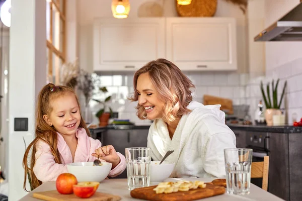 幸せな白人の大人の女性と子供の女の子は家でキッチンで朝食を持っています — ストック写真