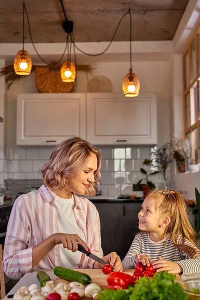 魅力的な若いシングルマザーが娘と一緒に台所でサラダを作る — ストック写真