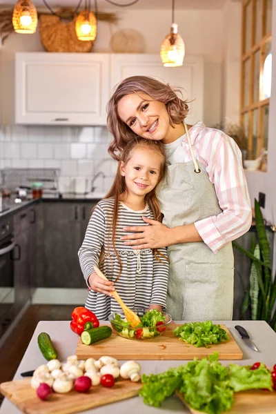Alegre niña preparando una ensalada con su madre en la cocina — Foto de Stock