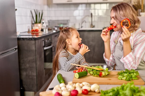 Cute mom and child girl tasting fresh fruits while preparing salad for dinner — Stock Photo, Image