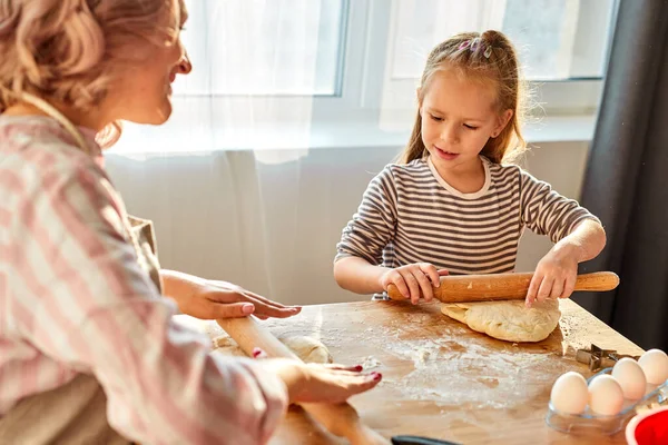 Cuidado mamá ayudar lindo sonriente pequeño preescolar hija rodando masa para galletas caseras —  Fotos de Stock