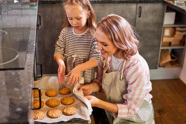 幸せな若い母親とかわいい子供の娘は台所でクッキーを焼く — ストック写真