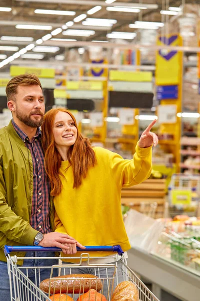 Gelukkig stel met winkelwagentje om eten te kopen bij supermarkt of supermarkt — Stockfoto