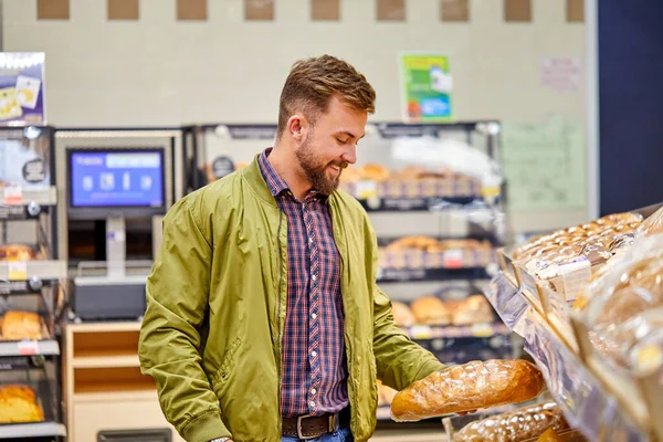 portrait of young caucasian male choosing bread in supermarket