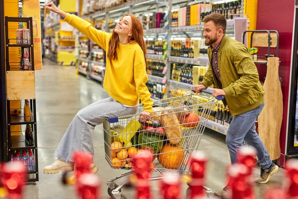 Sidovy på man driver kundvagn med redhedad kvinna sitter i den — Stockfoto