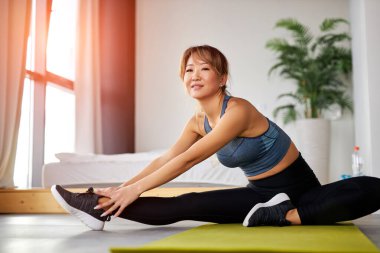 Esnek Asyalı kadın evde paspasın üzerinde geriniyor.