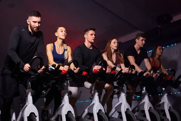 Grup de tineri musculoși care lucrează pe bicicleta de exerciții la sală — Fotografie, imagine de stoc