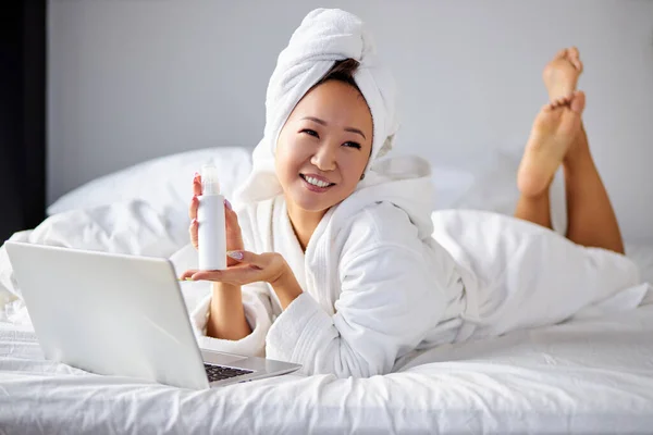 Mieszane rasy kobieta w szlafroku i ręcznik za pomocą laptopa podczas leżenia na wygodnym łóżku w domu — Zdjęcie stockowe