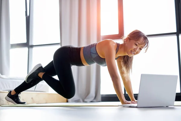Mujer joven en forma disfrutando de entrenamiento en la estera solo en casa, dando taller de pilates educativos en línea — Foto de Stock