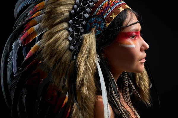 Allvarlig shamansk kvinna med indisk fjäder bär och färgglada makeup — Stockfoto