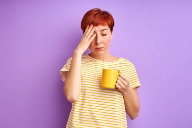 Kızıl saçlı kadın baş ağrısı çekiyor, elinde bardakla.