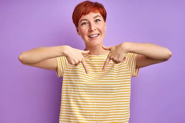 Pozitivní běloška zrzka žena ukazující prstem dolů — Stock fotografie