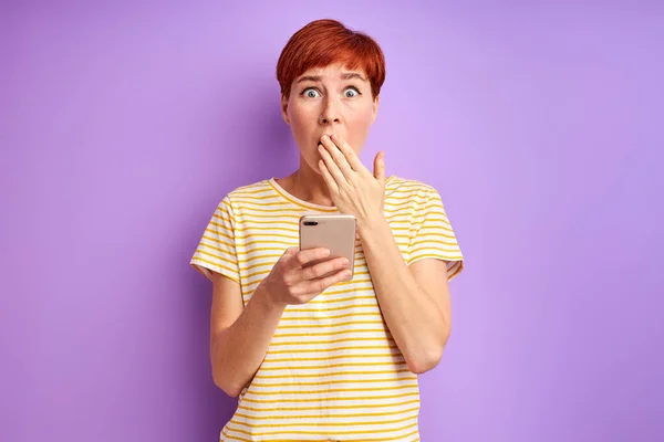 surprised redhead woman stand in shock by news on smartphone