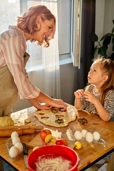 La madre caucásica y la hija preparan los productos de harina horneada en una mesa en la cocina en casa —  Fotos de Stock