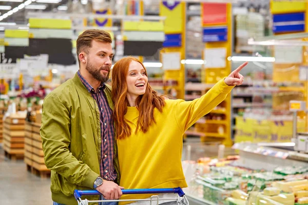 可爱的红头发女人在超市里给丈夫展示一些东西 — 图库照片
