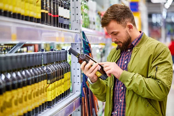 Zijaanzicht op klant mannelijke lezing wijnsamenstelling in supermarkt — Stockfoto