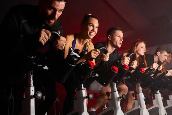 Σπορ γυναίκες και άνδρες σε μηχανή ποδηλασίας εργάζονται στο σύγχρονο γυμναστήριο ανυπομονούμε — Φωτογραφία Αρχείου