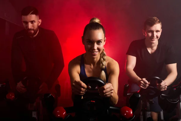 Caucasiano homens e mulheres em sportswear, treino andar de bicicleta no ginásio — Fotografia de Stock