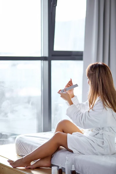 Азиатская красивая женщина подает свои ногти с папкой, сидя на кровати дома — стоковое фото