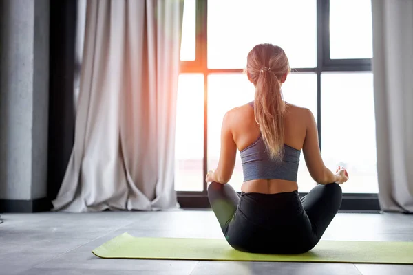 rear view on calm unrecognizable fit woman sitting in lotus pose