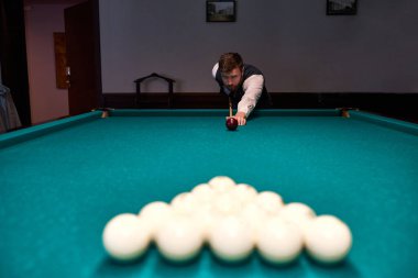 Adam bilardo masasında kolunu tutuyor, bilardo oynuyor ya da bilardo oynamaya hazırlanıyor.