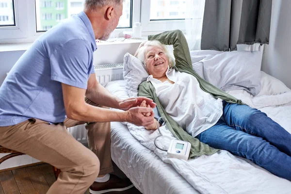 Feliz anciana paciente en el hospital con marido preocupado cogido de la mano — Foto de Stock