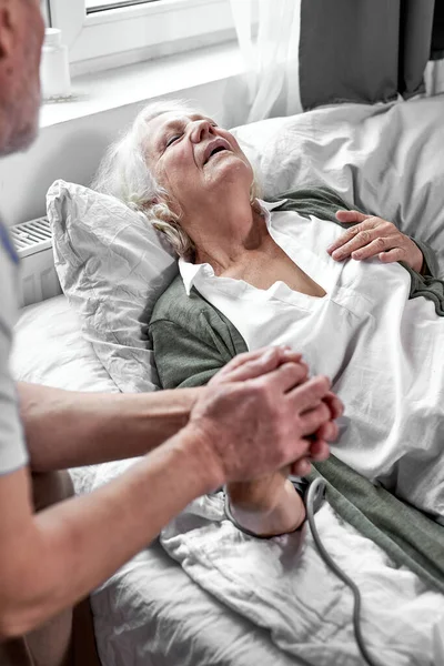 Amoroso hombre mayor apoyando a su esposa enferma en el hospital, sosteniendo su mano — Foto de Stock
