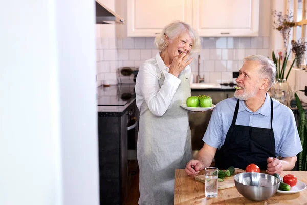 Porträtt av stilig senior man snida grönsaker och fru håller tallrik med äpplen — Stockfoto
