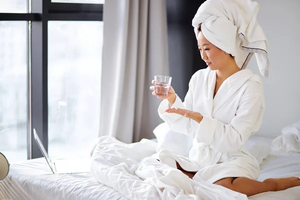 Coréenne prenant une pilule, assise sur son lit à la maison, portant peignoir et serviette — Photo