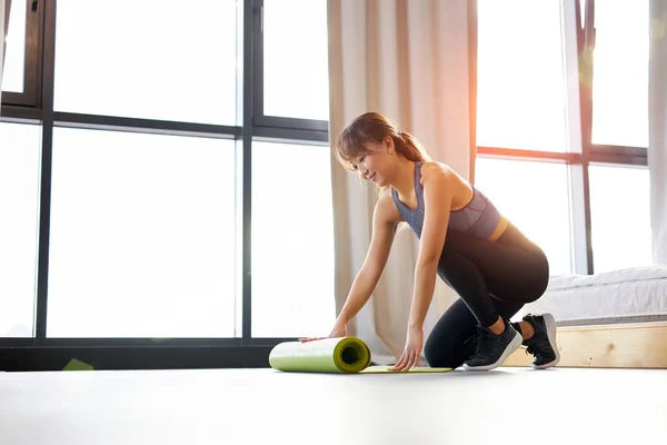 Joven atlética asiática mujer en ropa deportiva extiende una esterilla de yoga en el suelo por la mañana antes del ejercicio — Foto de Stock