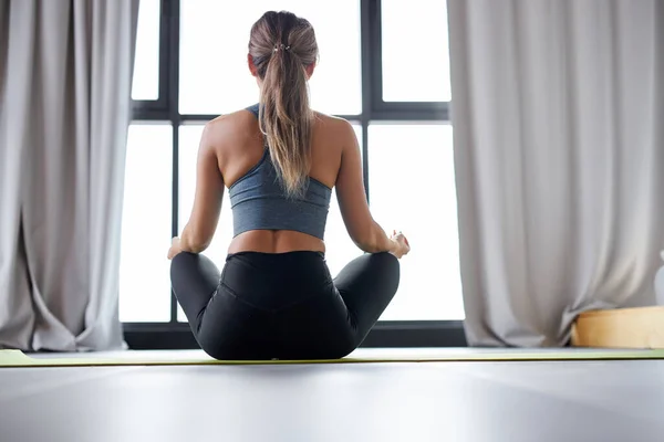 Mujer en top deportivo y polainas practicando yoga en casa sentada en pose de loto —  Fotos de Stock