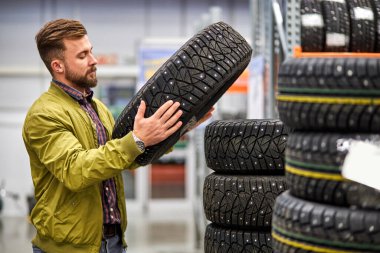 Yakışıklı adam dükkanda araba lastiği seçiyor.