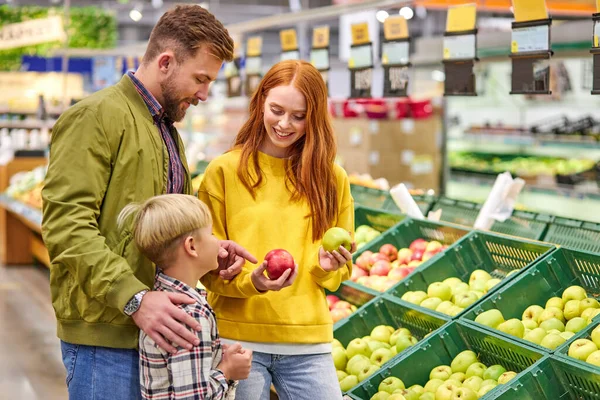 Groene of rode vrouw geeft het kind een keuze. paar met een kind kopen vruchten — Stockfoto