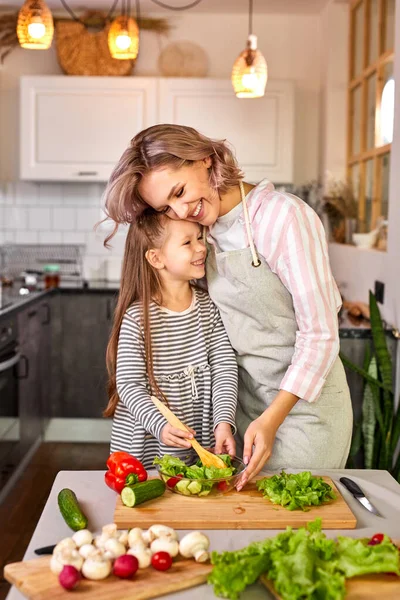 Χαρούμενο κορίτσι ετοιμάζει σαλάτα με τη μητέρα της στην κουζίνα. — Φωτογραφία Αρχείου
