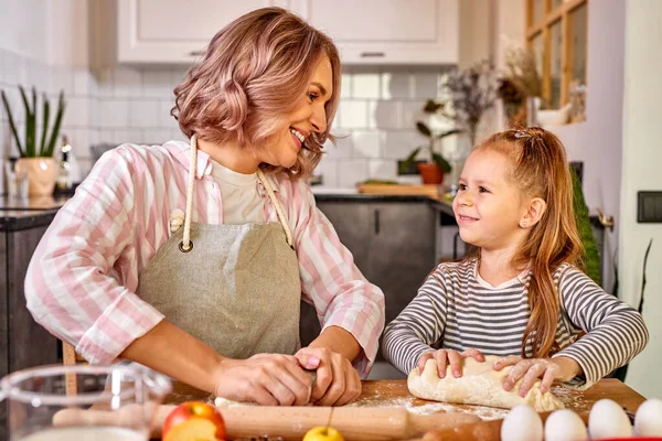 Menina e sua mãe no avental amassar a massa na cozinha — Fotografia de Stock