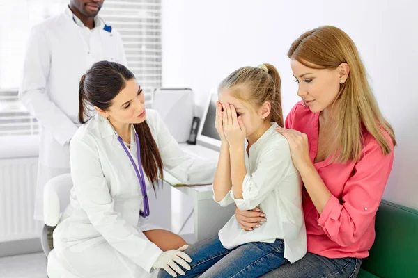 Young professional female doctor general practitioner talks and amuses child before medical examination — Foto Stock