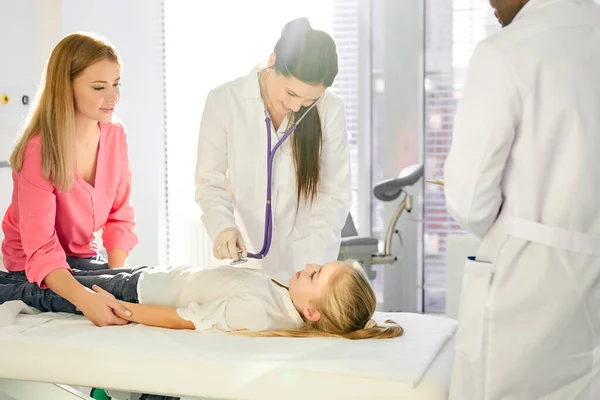 Vit kvinnlig läkare kontrollera hjärtslag med stetoskop medan hans afrikanska manliga kollega hjälpa henne — Stockfoto