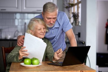 worried senior couple checking finances at home using laptop clipart