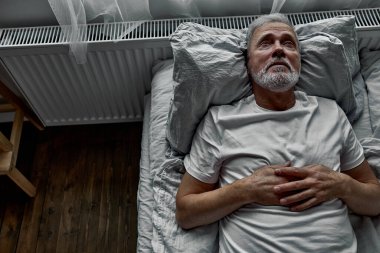 middle-aged man lying down in bed on pillow, having insomnia sleeping disorder