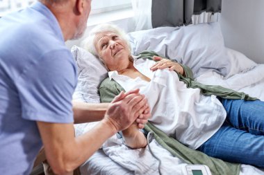 sick female patient at hospital with worried husband holding hands