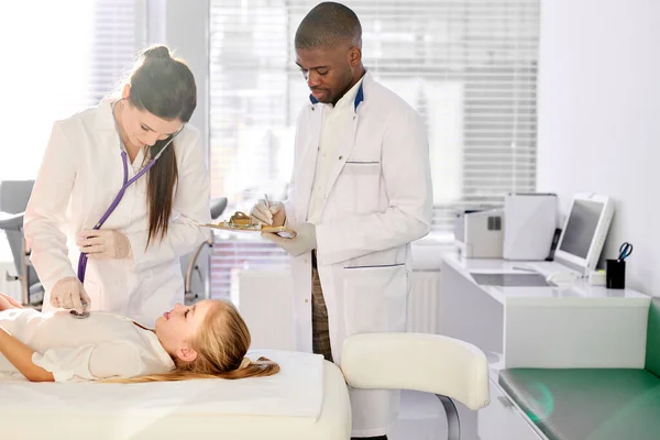 Friendly team of colleagues doctors examining health of girl patient — Stockfoto