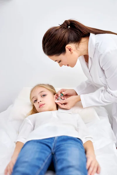 Piercing orejas a niña caucásica en el salón médico por un médico utilizando un dispositivo especial —  Fotos de Stock
