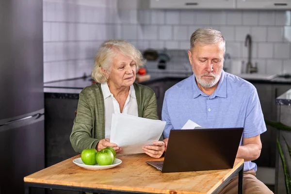 Worried senior couple checking finances at home using laptop — Fotografia de Stock